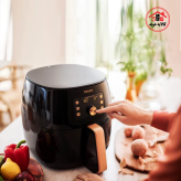 سرخ کن فیلیپس HD9867/90 که روی کانتر آشپزخانه است و خانمی در حال کار کردن با صفجه دیجیتالی آن است.